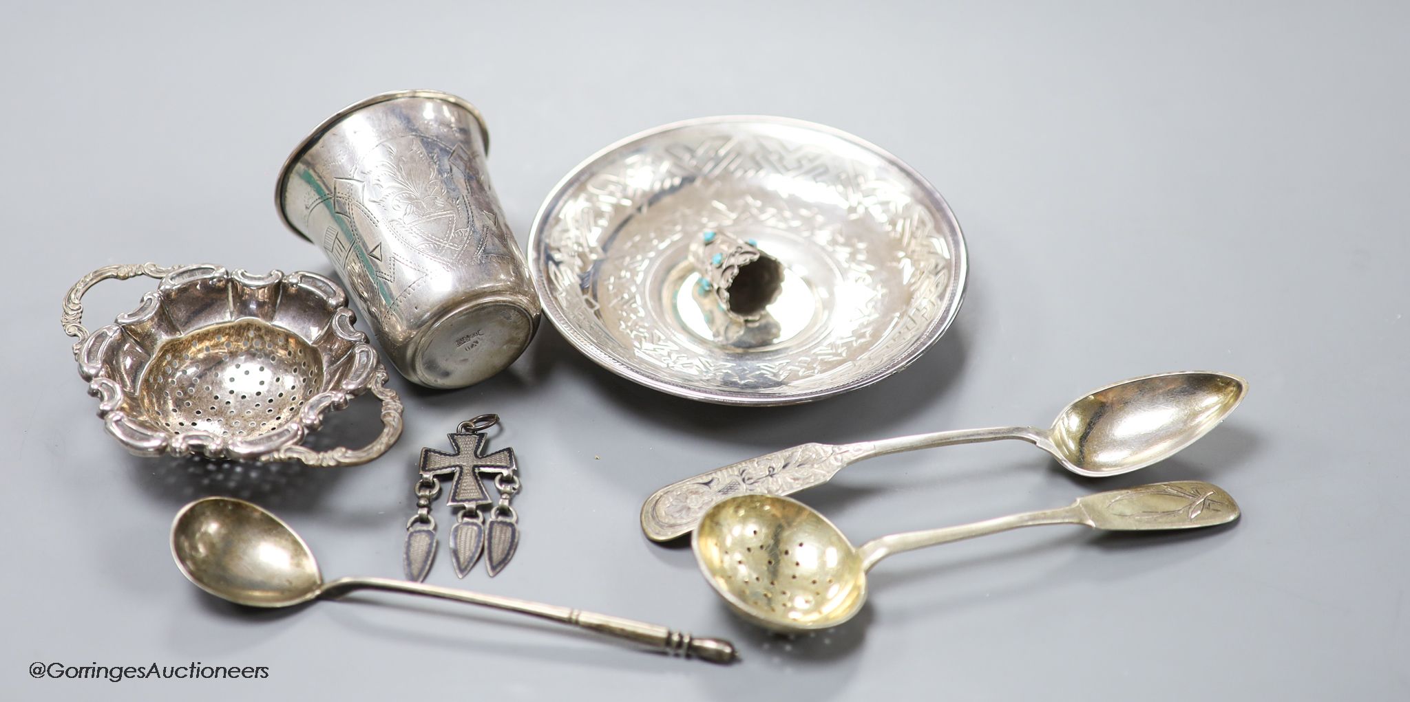 A late 19th century Russian engraved 84 zolotnik beaker, 1893, 63mm, a similar saucer, 1886, three assorted similar spoons, a white metal thimble and pendant and a German 835 tea strainer